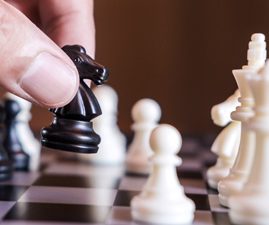A hand moves a knight across a chess board, representing a sacrifice made in the game.