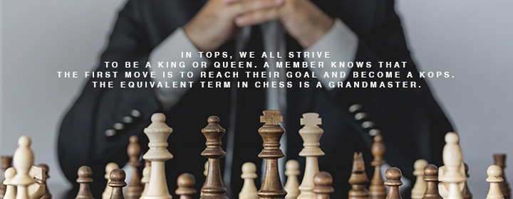 A man behind a chess board full of chess pieces.
"In TOPS, we all strive to be a King or Queen. A member knows that the equivalent term in chess in a grandmaster."