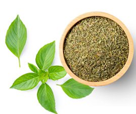 Basil herb dried in a bowl with fresh leaves scattered on a white table.
