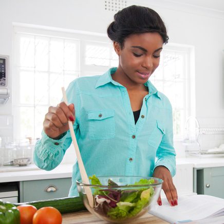 Female making lunch reading a cookbook.