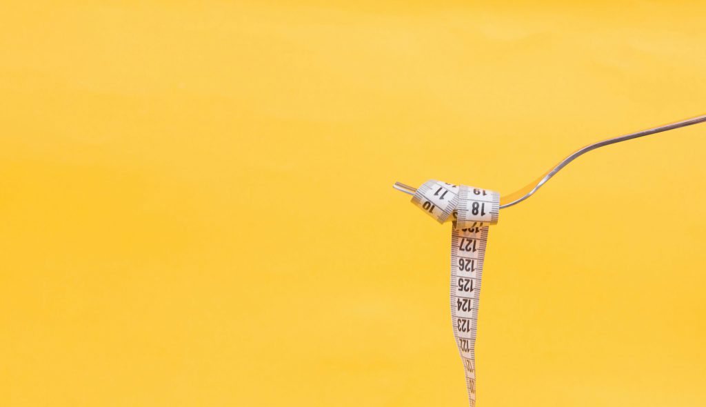 How many calories should you aim to eat in a day? Pictured: A tape measure wrapped around a fork over a yellow background.